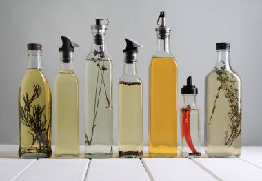 Bottles of different cooking oils on white wooden table against grey background