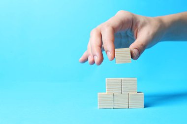 Açık mavi arkaplan üzerine küp piramidi inşa eden bir kadın, metin için yere yakın çekim yapıyor. Fikir kavramı