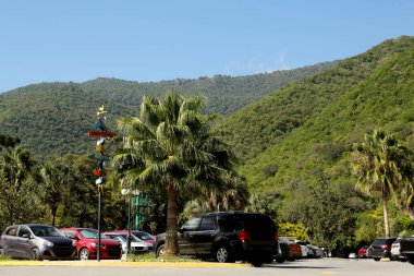 Dağların manzarası, palmiye ağaçları ve yol kenarında park edilmiş arabalar.