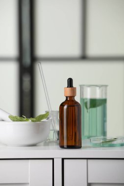 Beyaz laboratuvar çekmecesinde yaprakları olan şişe ve cam tüpler.