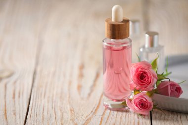 Beyaz ahşap masada bir şişe gül yağı ve çiçekler, metin için yer.