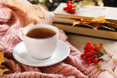 Bir fincan aromatik çay, yumuşak pembe kazak ve bej desenli masa üzerinde viburum. Sonbahar atmosferi