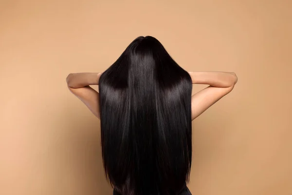 Woman with strong healthy hair on beige background, back view