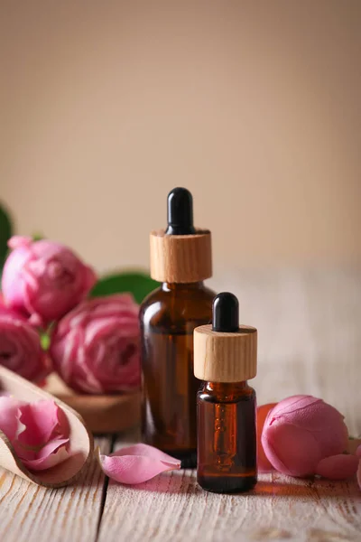 Flaschen Mit Ätherischem Und Rosen Auf Weißem Holztisch Vor Beigem — Stockfoto