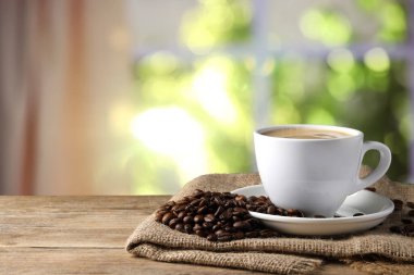 Bir fincan sıcak aromatik kahve ve ahşap masa üzerinde kavrulmuş fasulye.