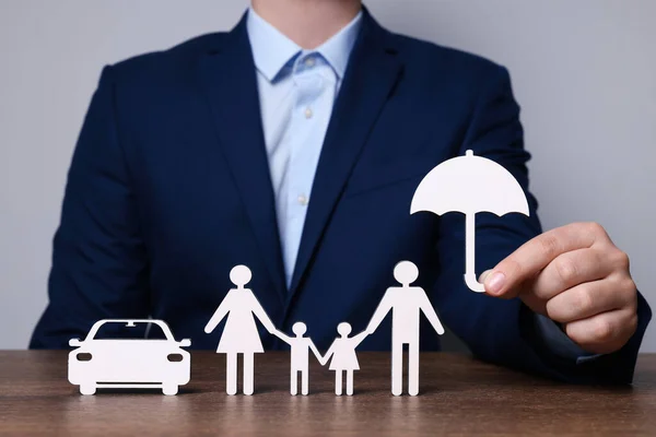 stock image Man holding figure of umbrella near family and car at wooden table. closeup. Insurance concept