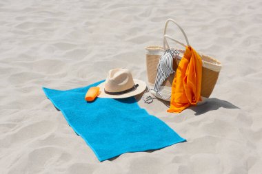 Blue towel, bag and beach accessories on sand clipart