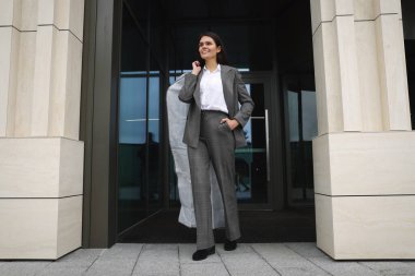 Çekici, mutlu bir iş kadını, açık havada giysi örtüsü tutuyor. Kuru temizleme servisi