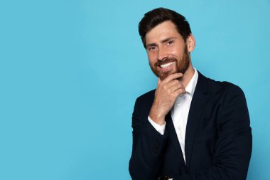 Açık mavi arka planda takım elbiseli gülümseyen sakallı adamın portresi.