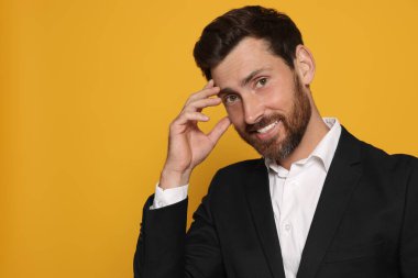 Turuncu arka planda takım elbiseli gülümseyen sakallı adamın portresi. Metin için boşluk