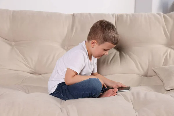 Boy with poor posture using phone on beige sofa indoors. Symptom of scoliosis