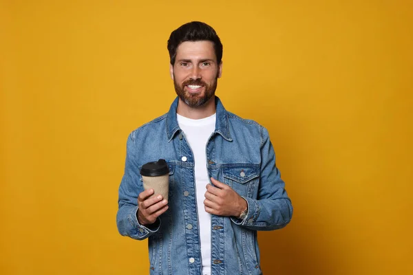 Smiling bearded man with paper cup of drink on orange background