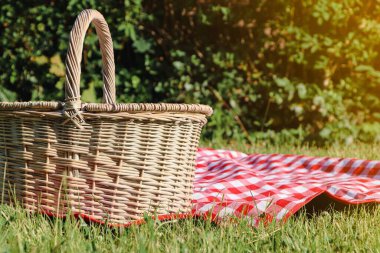 Picnic basket with checkered tablecloth on green grass outdoors, space for text