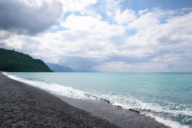 Güzel deniz kıyısı manzarası ve bulutlu gökyüzü altındaki dağlar.