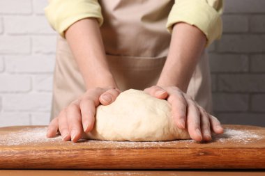 Beyaz tuğla duvarın yanındaki ahşap masada hamur yoğuran kadın, yakın plan.