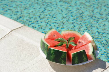 Slices of watermelon on white plate near swimming pool outdoors. Space for text