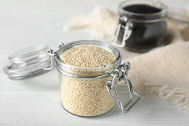 Beyaz ahşap masada susam tohumlu cam kavanozlar.