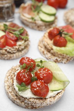 Krem peynirli çıtır karabuğday kekleri, domates ve salatalık dilimleri beyaz masada, yakın plan.