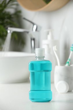 Banyodaki beyaz tezgahta gargara, diş fırçası ve diş ipi.