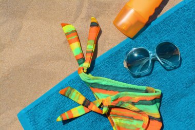 Yumuşak mavi plaj havlusu, güneş kremi şişesi, güneş gözlüğü ve renkli bikini tabanı, düz yatıyordu.