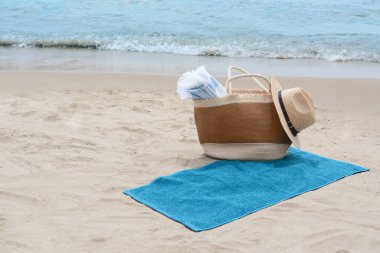 Battaniyeli çanta, plaj havlusu ve kumlu deniz kıyısında hasır şapka, mesaj için yer.