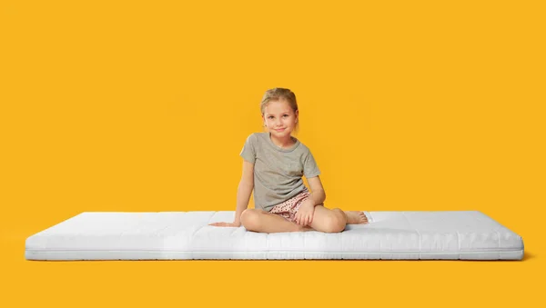 Kleines Mädchen Auf Matratze Vor Orangefarbenem Hintergrund — Stockfoto