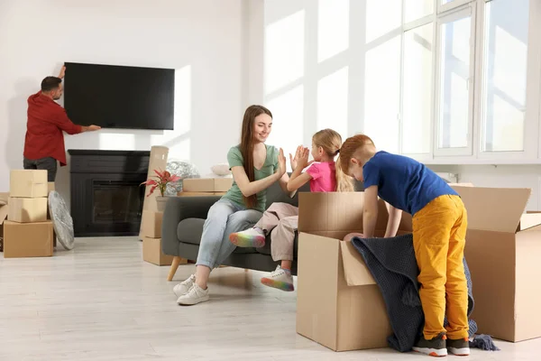 一家人安家了 爸爸打开电视 快乐的妈妈和女儿在沙发上玩耍 儿子打开他的盒子 搬家日 — 图库照片
