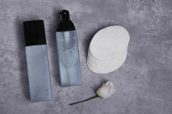 Luxury cosmetic products, cotton pads and flower on grey table, flat lay