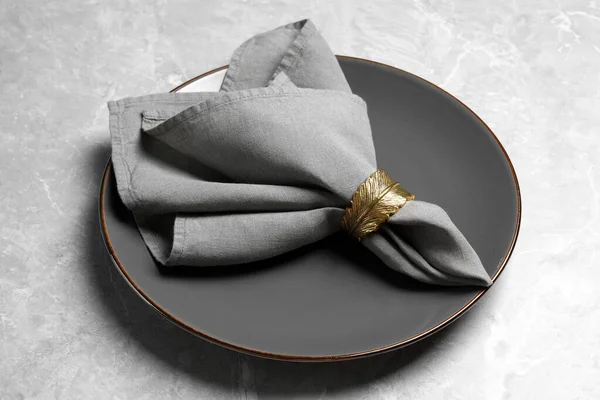 Plate with fabric napkin and decorative ring on gray marble table