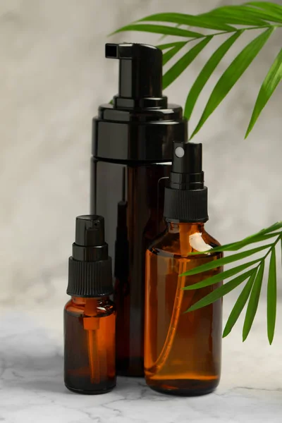 Bottles of organic cosmetic products and green leaves on light marbled background