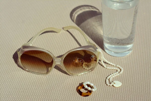 Κομψά Γυαλιά Ηλίου Ποτήρι Νερό Και Κοσμήματα Γκρι Επιφάνεια Closeup — Φωτογραφία Αρχείου