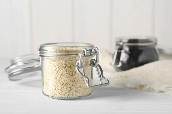 Glass jars with sesame seeds on white wooden table