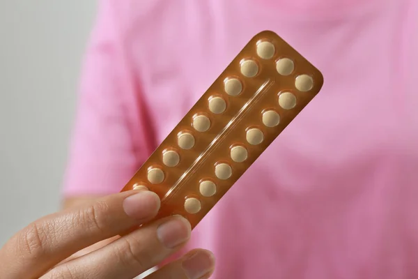 Woman holding birth control pills on grey background, closeup