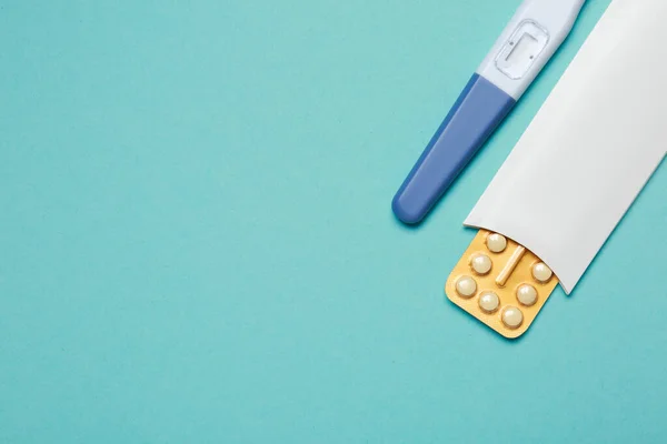 Birth control pills and pregnancy test on light blue background, top view. Space for text