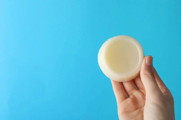 Woman holding solid shampoo bar against light blue background, closeup. Space for text