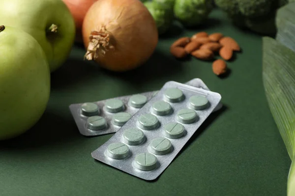 Blisters with pills and food on green background, closeup. Prebiotic supplements