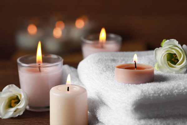 Beautiful spa composition with burning candles and flowers on wooden table, closeup