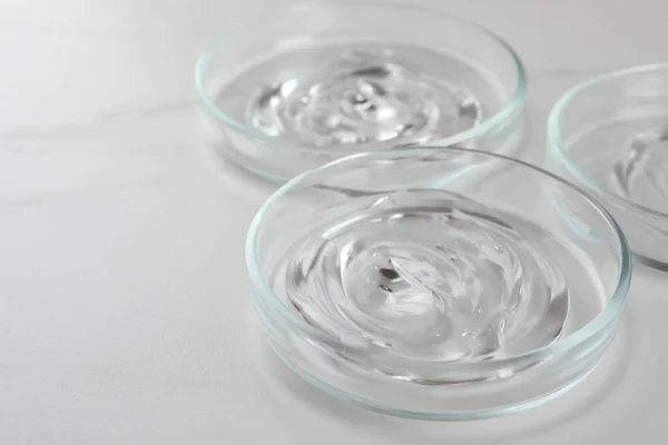 Petri dishes with liquids on white marble table, closeup. Space for text