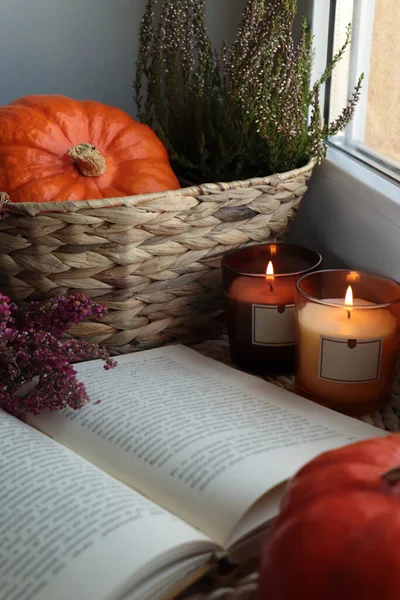 stock image Wicker basket with beautiful heather flowers, pumpkin, burning candles and open book near window indoors