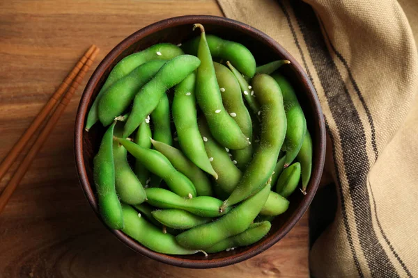 Green edamame beans in pods served on wooden table, flat lay