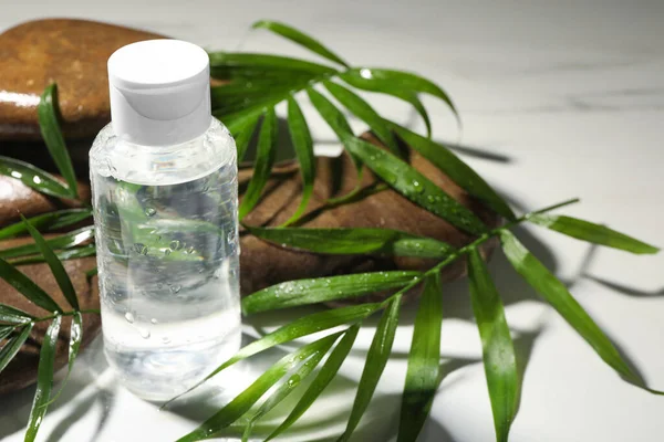 stock image Bottle of micellar cleansing water, green twigs and spa stones on white table, closeup. Space for text