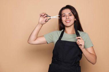 Profesyonel makasla mutlu bir kuaför portresi ve soluk turuncu arka planda tarak. Metin için boşluk