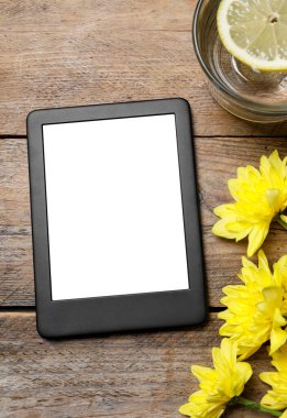 Kasımpatı yakınında modern e-kitap okuyucu ve ahşap masanın üzerinde bir bardak limon suyu, düz yatıyordu.