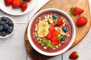 Taze böğürtlen, muz ve granola içeren nefis meyve suyu kasesi fayanslı yüzeyde, düz bir şekilde yatıyordu.