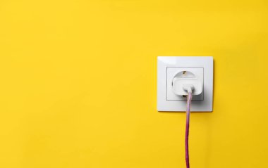 Sarı duvardaki güç prizine takılı şarj adaptörü, metin için boşluk. Elektrik arzı