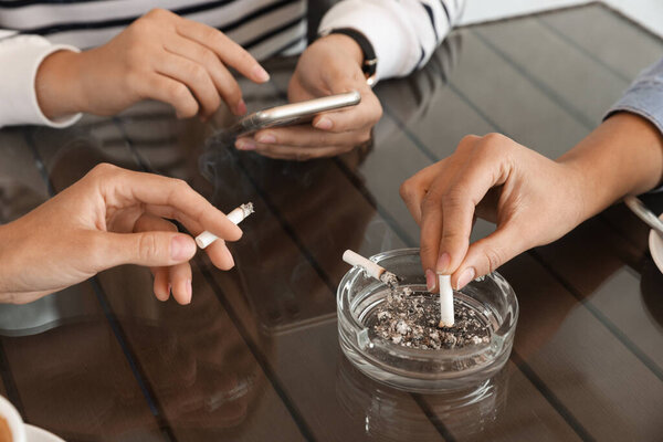 Женщина бросает сигарету в пепельницу за столом, крупным планом