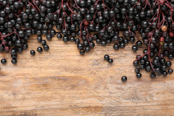Black elderberries (Sambucus) on wooden table, flat lay. Space for text
