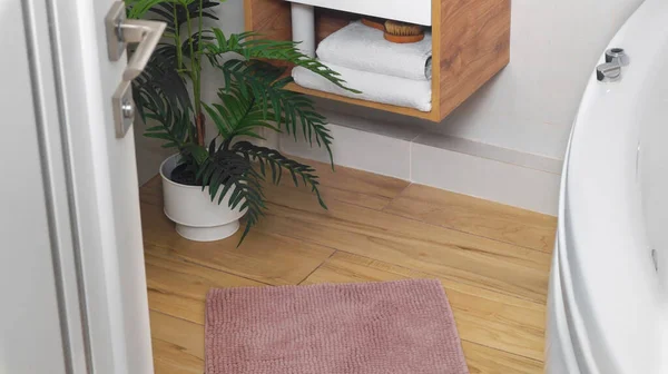 Soft bath mat near houseplant on wooden floor in bathroom