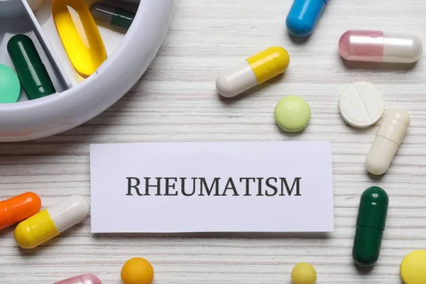 stock image Card with word Rheumatism and pills on white wooden table, flat lay