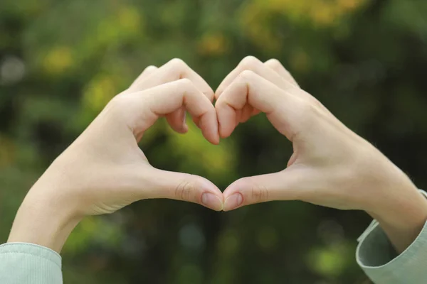 Woman making heart with hands outdoors, closeup